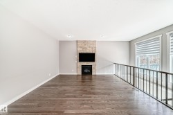 Open-concept living area featuring rich wood-finish flooring, a stone-clad fireplace with mounted television, recessed lighting, and a contemporary metal railing - 