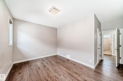 Spacious room featuring wood-finish flooring, neutral wall tones, a modern flush-mount light fixture, and white trim - 