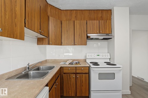 Kitchen featuring wood-finish cabinetry, white tile backsplash, a double basin stainless steel sink, and a white electric range with an overhead vent - 11147 78 Avenue Nw, Edmonton, AB 
