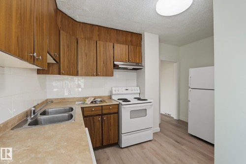 Kitchen featuring wood-finish cabinetry, laminate countertops, a stainless steel double sink, white tile backsplash, and light wood-finish flooring - 11147 78 Avenue Nw, Edmonton, AB 