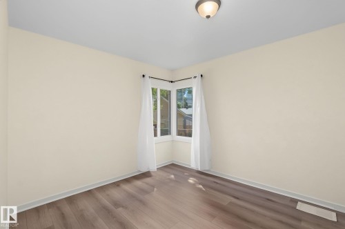 Corner window allowing natural light, wood-finish flooring, light-toned walls, white trim, and a ceiling-mounted light fixture - 11147 78 Avenue Nw, Edmonton, AB 
