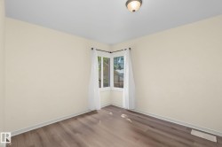 Corner window allowing natural light, wood-finish flooring, light-toned walls, white trim, and a ceiling-mounted light fixture - 