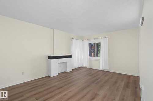 Spacious room featuring wood-finish flooring, a decorative fireplace with a dark mantel, and ample natural light from a large window - 11147 78 Avenue Nw, Edmonton, AB 