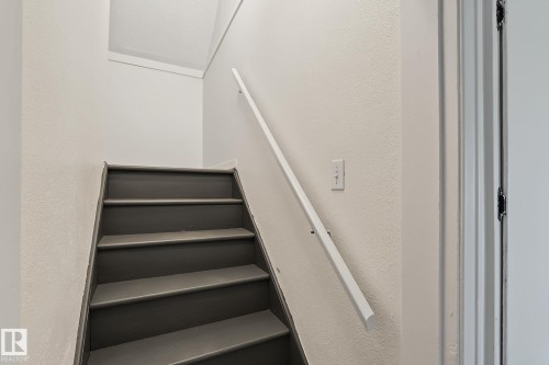 Staircase featuring dark gray treads, white risers, a white handrail, and light-colored textured walls - 11147 78 Avenue Nw, Edmonton, AB 