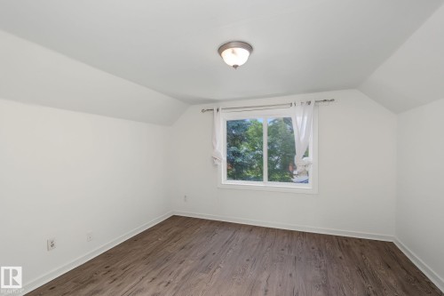 Room featuring sloped ceilings, white painted walls, and wood-finish flooring - 11147 78 Avenue Nw, Edmonton, AB 