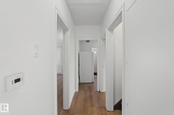 Hallway featuring wood-finish flooring, white walls, and multiple doorframes - 