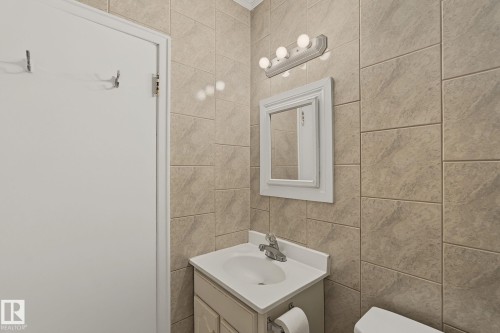 Bathroom featuring floor-to-ceiling rectangular wall tiles, a single vanity with an integrated sink and chrome faucet, and a wall-mounted mirror with a decorative frame - 11147 78 Avenue Nw, Edmonton, AB 