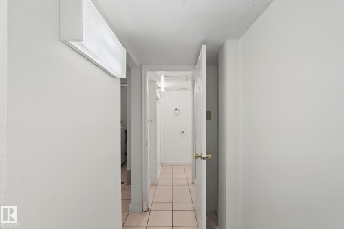 Hallway featuring white walls, a textured ceiling, a flush-mounted fluorescent light fixture, and a tile floor - 11147 78 Avenue Nw, Edmonton, AB 