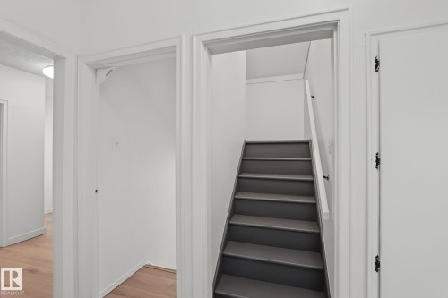 Staircase with gray treads and a white handrail, framed by white walls and doorways - 11147 78 Avenue Nw, Edmonton, AB 