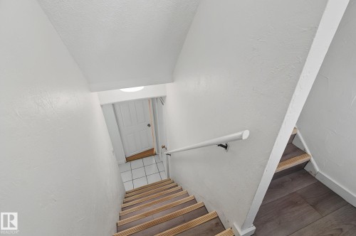 Stairwell featuring wood-finish treads, a white wall-mounted handrail, and white painted walls - 11147 78 Avenue Nw, Edmonton, AB 