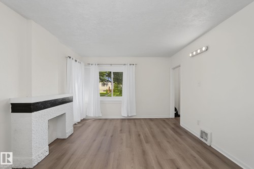Living space featuring wood-finish flooring, a white textured fireplace with a dark mantel, and a window providing natural light - 11147 78 Avenue Nw, Edmonton, AB 