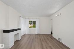 Living space featuring wood-finish flooring, a white textured fireplace with a dark mantel, and a window providing natural light - 