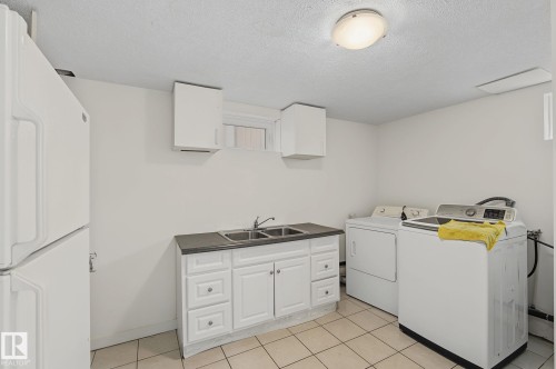 Utility room featuring a double basin sink, white cabinetry with silver hardware, and light-toned tile flooring - 11147 78 Avenue Nw, Edmonton, AB 