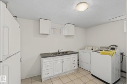 Utility room featuring a double basin sink, white cabinetry with silver hardware, and light-toned tile flooring - 