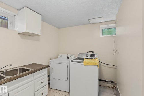 Utility room featuring a double basin sink, white cabinetry with silver hardware, and a window for natural light - 11147 78 Avenue Nw, Edmonton, AB 