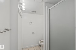 Bathroom featuring a frosted glass shower enclosure, a wall-mounted light fixture with three bulbs, and neutral-toned floor tiling - 