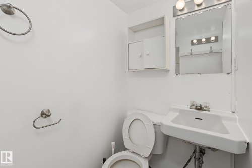 Compact bathroom featuring a wall-mounted sink, toilet, mirrored medicine cabinet, and wall-mounted storage cabinet - 11147 78 Avenue Nw, Edmonton, AB 