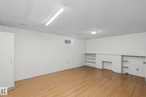 Spacious room featuring wood-finish flooring, a built-in white brick structure with shelving, and overhead fluorescent lighting - 11147 78 Avenue Nw, Edmonton, AB 