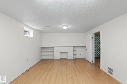 Spacious room featuring wood-finish flooring, white walls, and a built-in white brick fireplace surround with flanking shelving - 11147 78 Avenue Nw, Edmonton, AB 