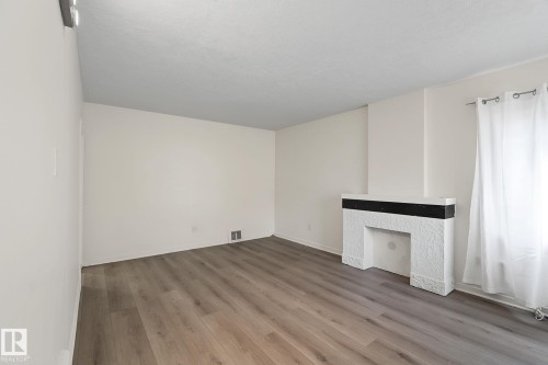 Spacious room featuring wood-finish flooring, a textured white fireplace with a dark mantel, and recessed lighting - 11147 78 Avenue Nw, Edmonton, AB 