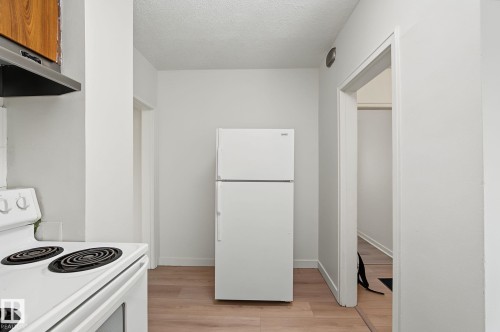 Kitchen area featuring a white top-freezer refrigerator, white electric range, and wood-finish flooring - 11147 78 Avenue Nw, Edmonton, AB 