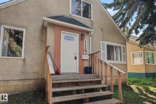 Front entry featuring a white paneled door with an arched glass insert, flanked by vertical wood-tone siding - 11147 78 Avenue Nw, Edmonton, AB 