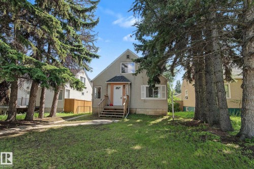 Front exterior featuring a light-colored facade, prominent pitched roofline, white entry door with decorative glass, and a wooden front porch and steps - 11147 78 Avenue Nw, Edmonton, AB 