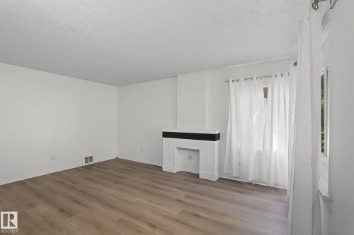 Living area featuring wood-finish flooring, white walls, and a white textured fireplace with a black mantel - 11147 78 Avenue Nw, Edmonton, AB 