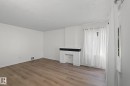 Living area featuring wood-finish flooring, white walls, and a white textured fireplace with a black mantel - 11147 78 Avenue Nw, Edmonton, AB  - Indoor Photo Showing Other Room 