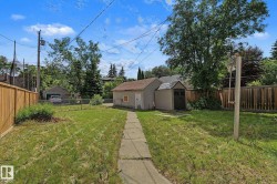 Expansive backyard featuring a concrete pathway, a detached single-car garage, and a garden shed - 