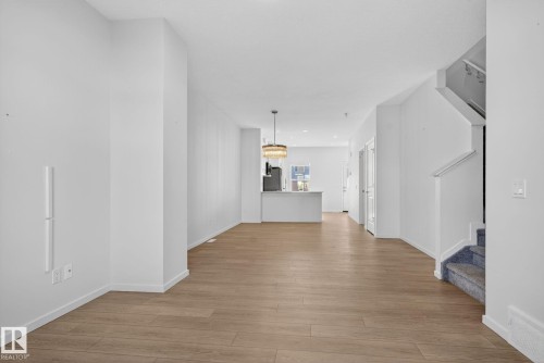 Open-concept main level featuring wood-finish flooring, white baseboards, and a modern chandelier - 264 Orchards Boulevard Sw, Edmonton, AB - Indoor Photo Showing Other Room