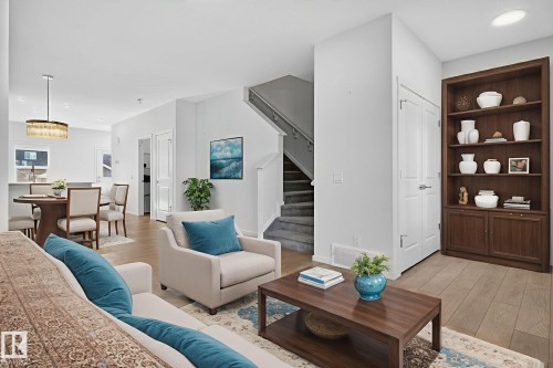 Open-concept living space featuring light wood-finish flooring, white walls, and a built-in dark wood bookcase - 264 Orchards Boulevard Sw, Edmonton, AB - Indoor Photo Showing Living Room
