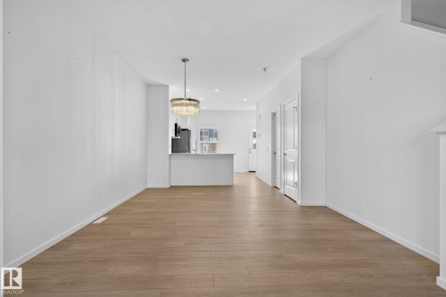 Open-concept living area featuring wood-finish flooring, white walls, and a contemporary chandelier - 264 Orchards Boulevard Sw, Edmonton, AB - Indoor