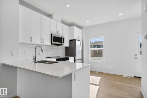 Modern kitchen featuring white shaker cabinetry, stainless steel appliances, a subway tile backsplash, and light wood-finish flooring - 264 Orchards Boulevard Sw, Edmonton, AB - Indoor Photo Showing Kitchen With Double Sink With Upgraded Kitchen