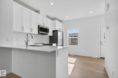 Contemporary kitchen featuring white cabinetry, stainless steel appliances, a subway tile backsplash, and light wood-finish flooring - 264 Orchards Boulevard Sw, Edmonton, AB - Indoor Photo Showing Kitchen With Upgraded Kitchen