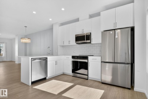 Modern kitchen featuring white cabinetry, stainless steel appliances, and wood-finish flooring - 264 Orchards Boulevard Sw, Edmonton, AB - Indoor Photo Showing Kitchen