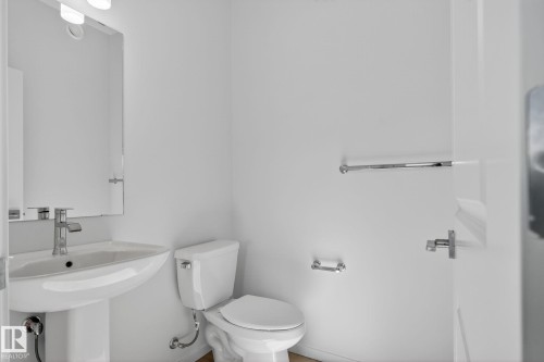 Powder room featuring a pedestal sink with chrome fixtures, a wall-mounted rectangular mirror, and a contemporary vanity light - 264 Orchards Boulevard Sw, Edmonton, AB - Indoor Photo Showing Bathroom