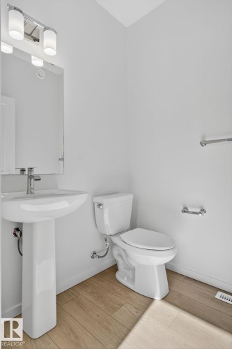 Powder room featuring a pedestal sink, a wall-mounted mirror, and a three-light vanity fixture - 264 Orchards Boulevard Sw, Edmonton, AB - Indoor Photo Showing Bathroom