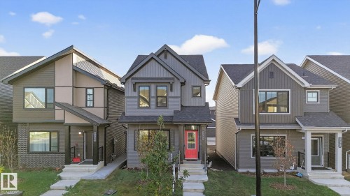 Contemporary gray siding residence featuring a bold red entry door, a covered front porch, and black-framed windows - 264 Orchards Boulevard Sw, Edmonton, AB - Outdoor With Facade