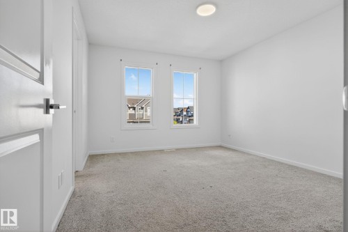 Bright interior room featuring a light-colored carpet, two double-hung windows, a flush-mount ceiling light fixture, and white trim - 264 Orchards Boulevard Sw, Edmonton, AB - Indoor Photo Showing Other Room