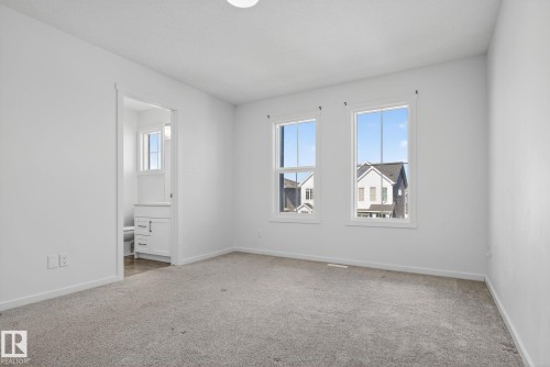 Carpeted room featuring two large windows, white walls, and a ceiling light fixture - 264 Orchards Boulevard Sw, Edmonton, AB - Indoor Photo Showing Other Room