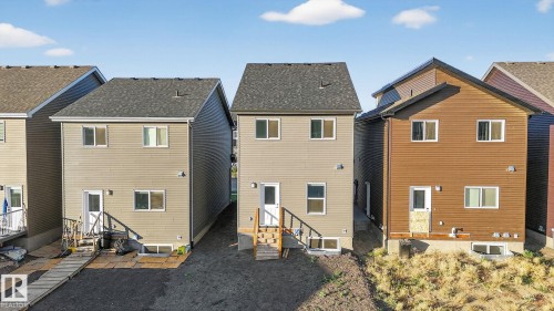 Rear exterior of a modern two-story home featuring light brown siding and a dark shingled roof - 264 Orchards Boulevard Sw, Edmonton, AB - Outdoor With Exterior