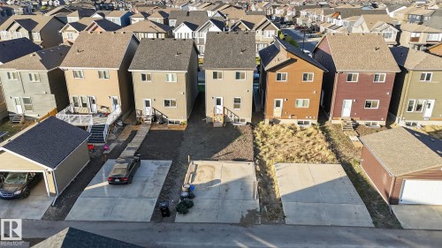 Rear exterior featuring light-colored siding, a white deck with stairs, a concrete patio, and a detached garage with a dark shingle roof - 264 Orchards Boulevard Sw, Edmonton, AB - Outdoor