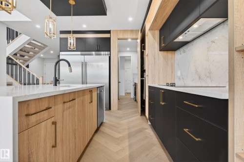 Contemporary kitchen featuring a large waterfall island with integrated sink and matte black faucet, herringbone wood-finish flooring, and two-tone cabinetry with gold-tone hardware - 431 172 Avenue, Edmonton, AB - Indoor Photo Showing Kitchen