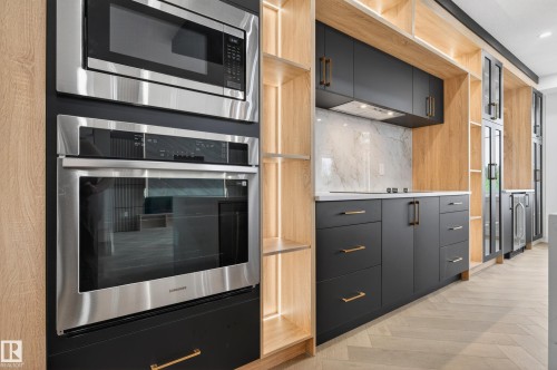 Modern kitchen featuring integrated stainless steel appliances, contrasting dark cabinetry with brass hardware, light wood-finish open shelving, a white marble-patterned backsplash, and light-toned wood-finish flooring - 431 172 Avenue, Edmonton, AB - Indoor Photo Showing Kitchen