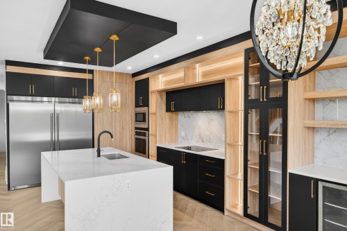 Gourmet kitchen featuring a waterfall island with an undermount sink, stainless steel appliances, black and wood-finish cabinetry, and a large crystal chandelier - 431 172 Avenue, Edmonton, AB - Indoor Photo Showing Kitchen With Upgraded Kitchen