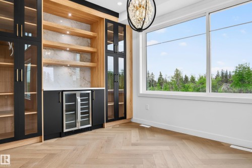 Custom built-in cabinetry featuring black glass-front doors with gold-toned hardware, wood-finish shelving, and a beverage cooler - 431 172 Avenue, Edmonton, AB - Indoor Photo Showing Other Room