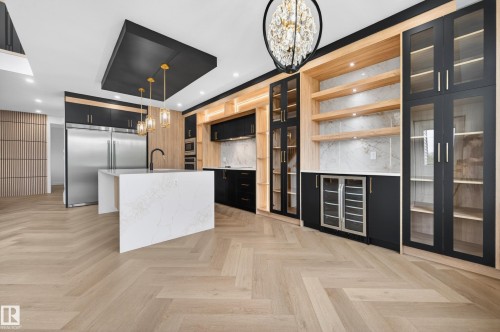Modern kitchen featuring light wood-finish herringbone flooring, a waterfall island with a white stone-finish countertop, and black cabinetry with gold-tone hardware - 431 172 Avenue, Edmonton, AB - Indoor Photo Showing Kitchen