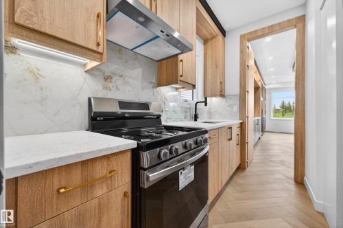 Modern kitchen featuring a stainless steel range with overhead ventilation, stone countertops, and a full-height stone backsplash - 431 172 Avenue, Edmonton, AB - Indoor Photo Showing Kitchen
