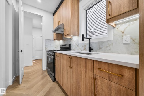 Modern kitchen featuring wood-finish cabinetry, white countertops, and a white and gold veined backsplash - 431 172 Avenue, Edmonton, AB - Indoor Photo Showing Kitchen